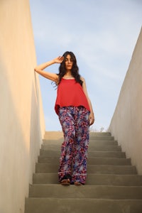 a woman in a red top and patterned pants standing on stairs